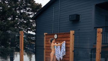 A swimming pool with a wooden deck area, a sauna, and a dark-colored building with a clock.