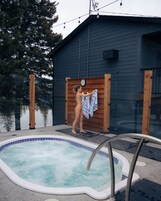 A swimming pool with a wooden deck area, a sauna, and a dark-colored building with a clock.