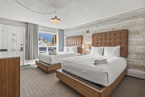 A hotel room with two beds, a wooden headboard, a large window with a view, and a hanging light fixture.