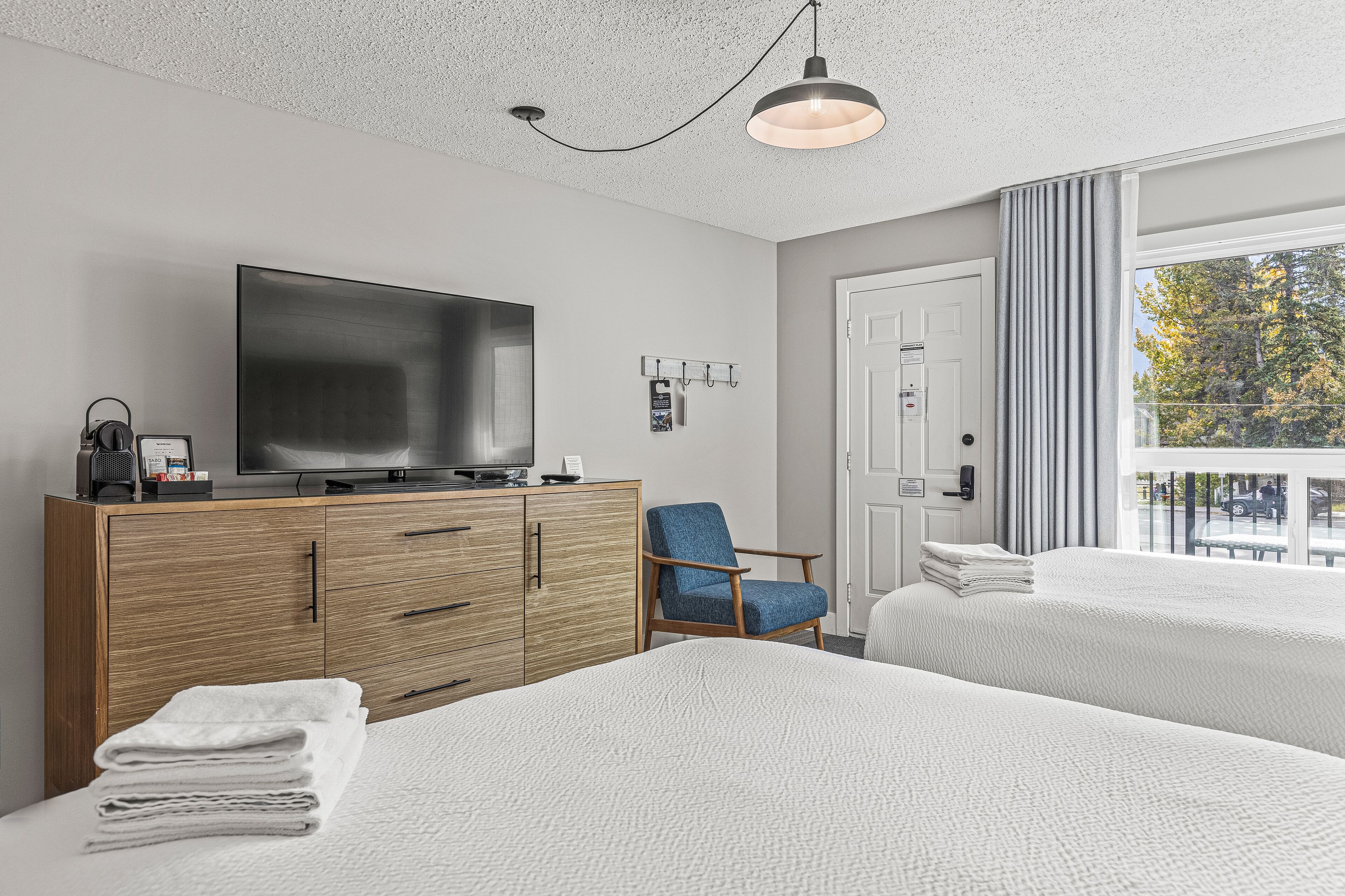 Une chambre d’hôtel avec deux lits, une télévision, une commode en bois, une chaise et une fenêtre donnant sur un paysage agréable.