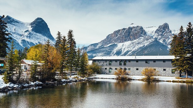 A building with a snow-covered roof, surrounded by mountains and trees. - Lamphouse By Basecamp (Canmore)