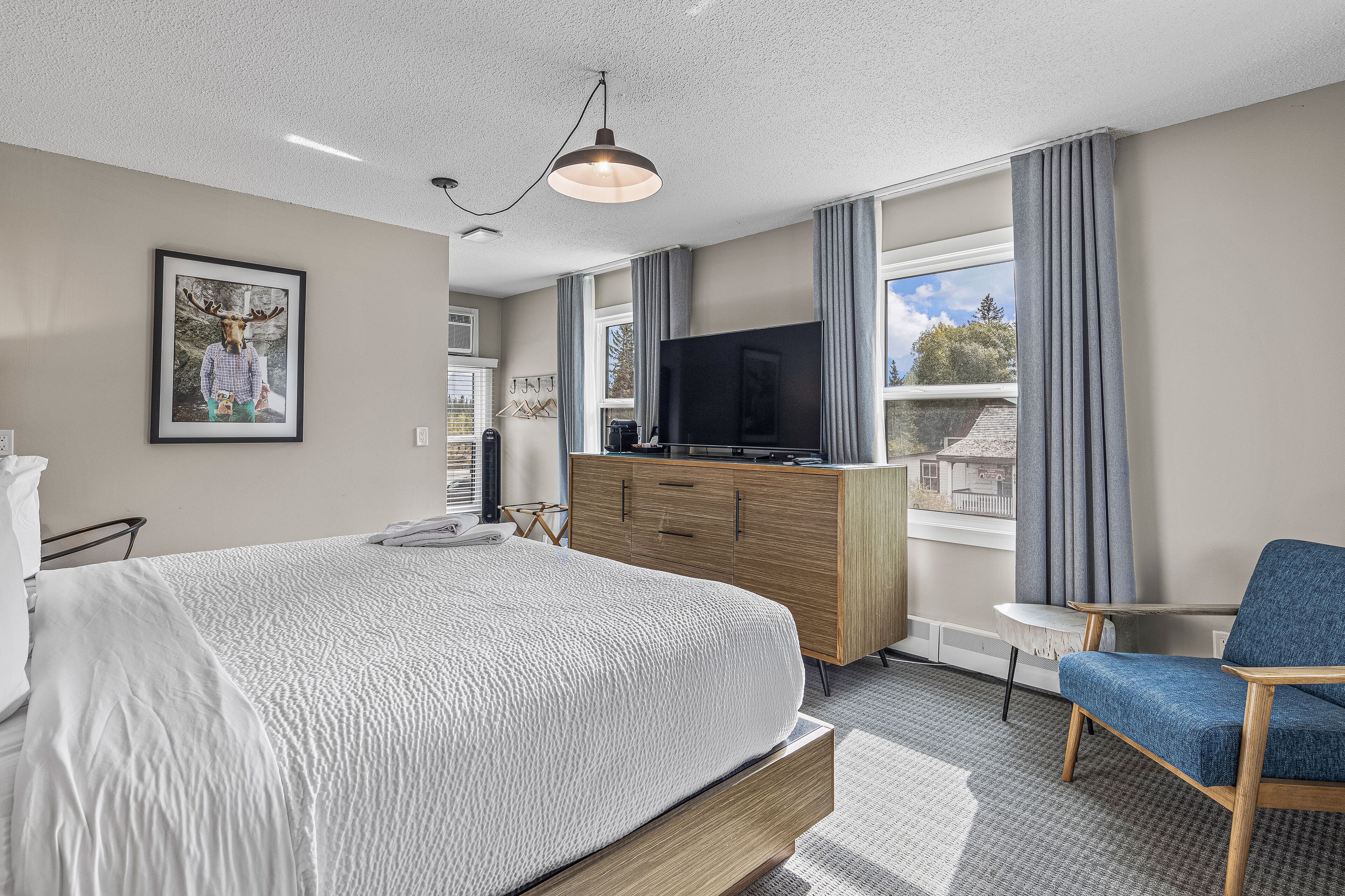Una habitación de hotel moderna con una cama grande, televisión, cómoda de madera y vistas a la ciudad.