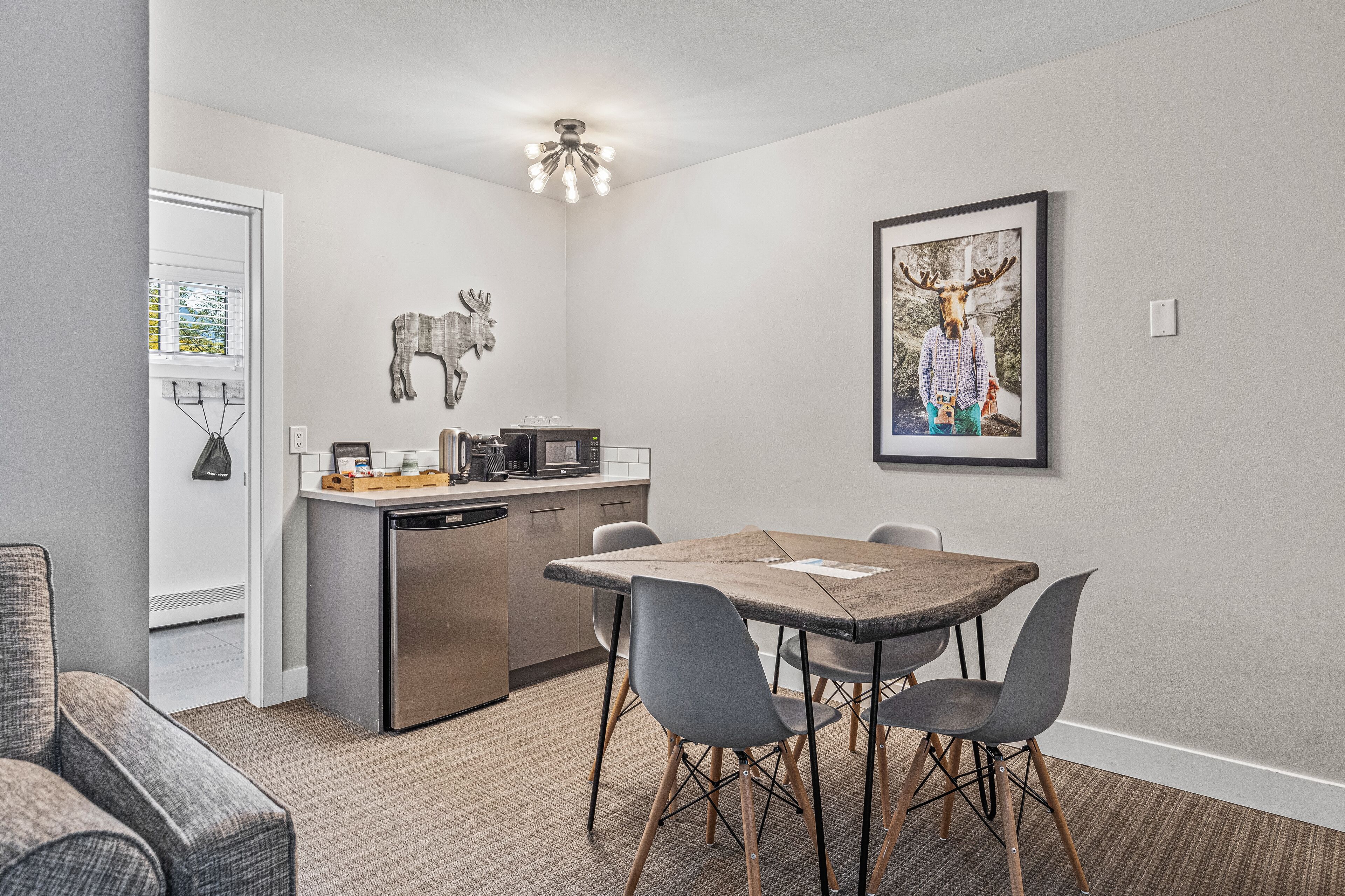 A compact kitchen with modern appliances, a dining area with a wooden table and chairs, and a mounted artwork of a moose.