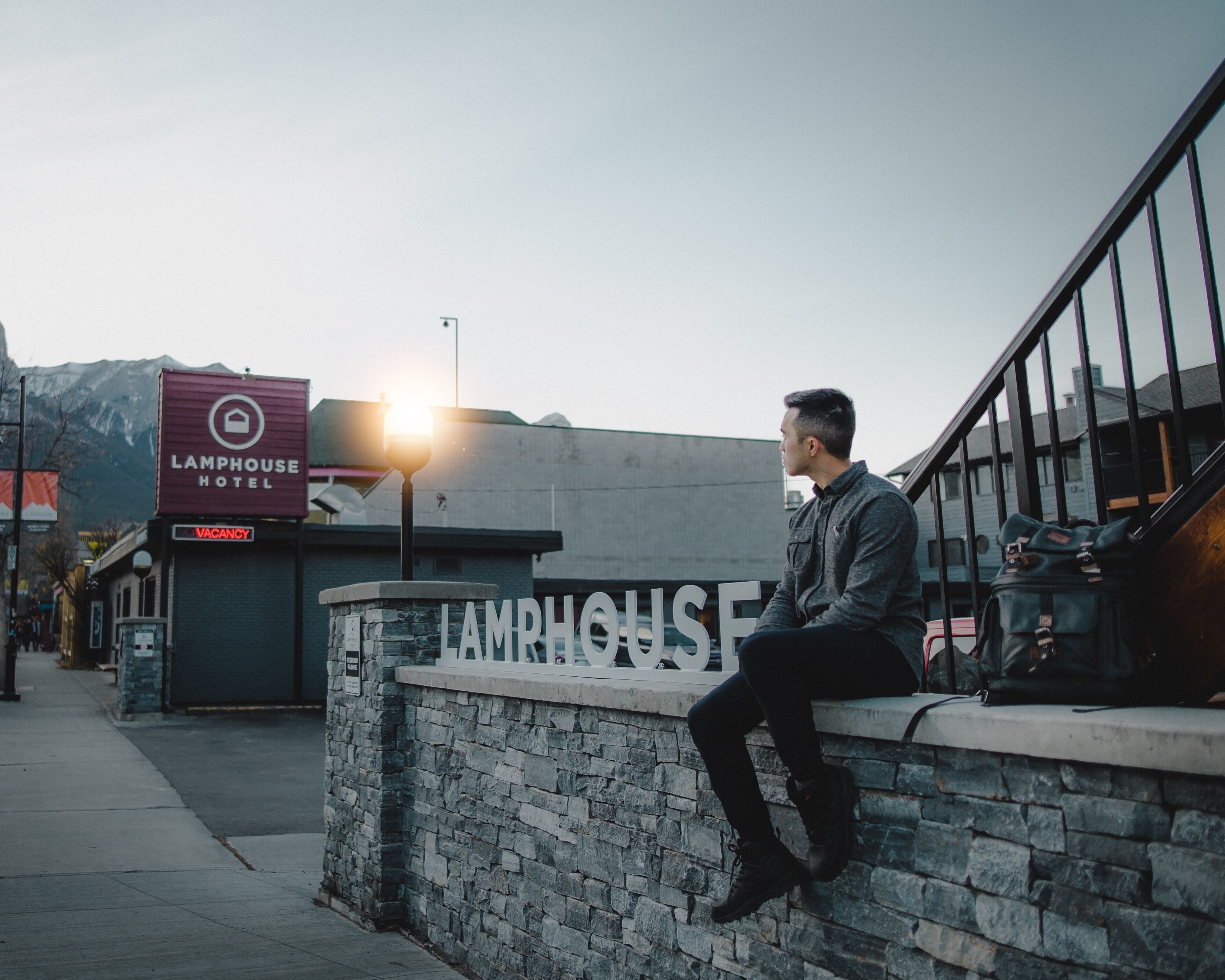 A man sitting on a stone wall outside a building with a sign that reads "LAMPHOUSE HOTEL".