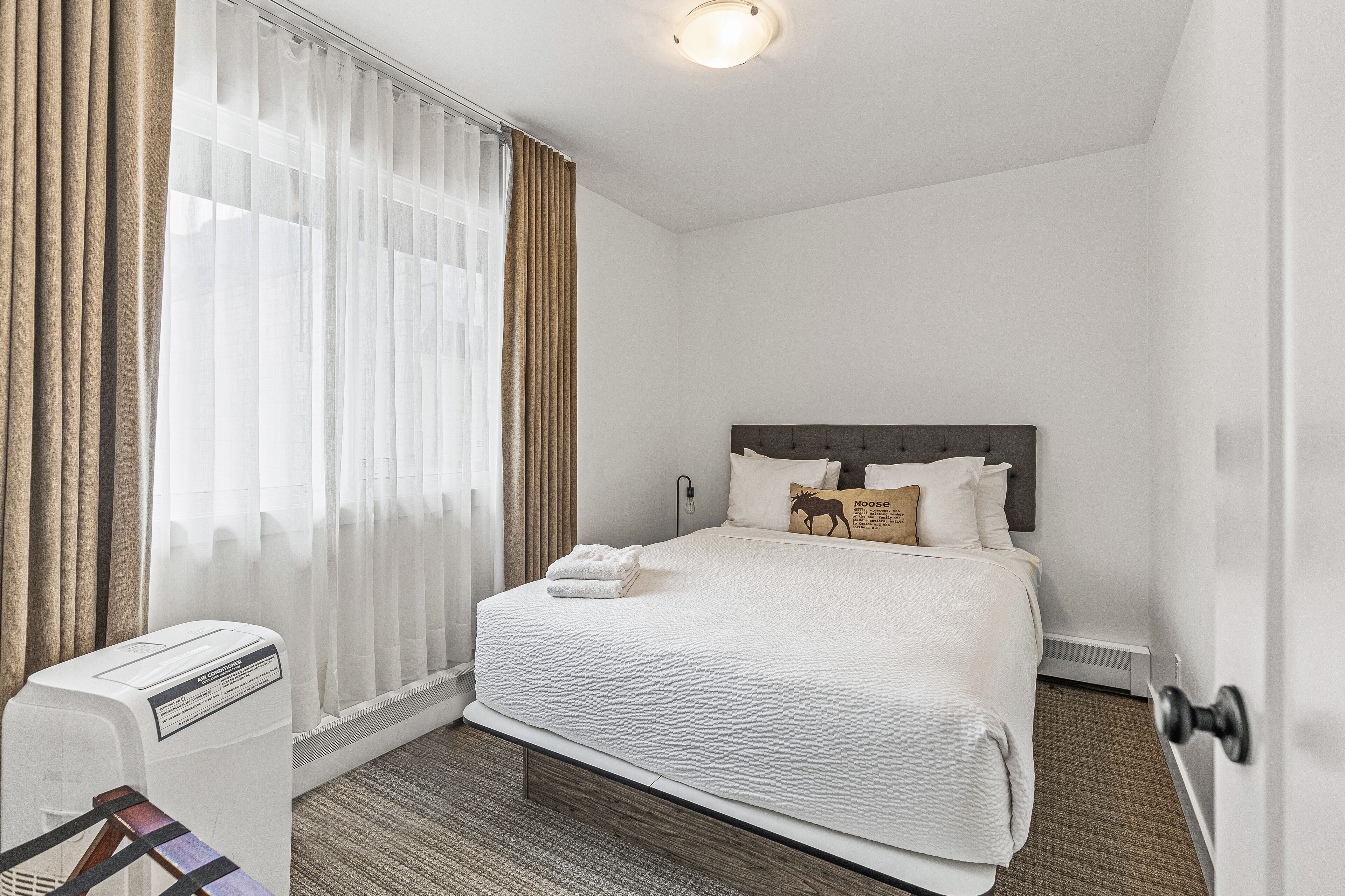 A hotel room with a large bed, a heater, and a window with curtains.