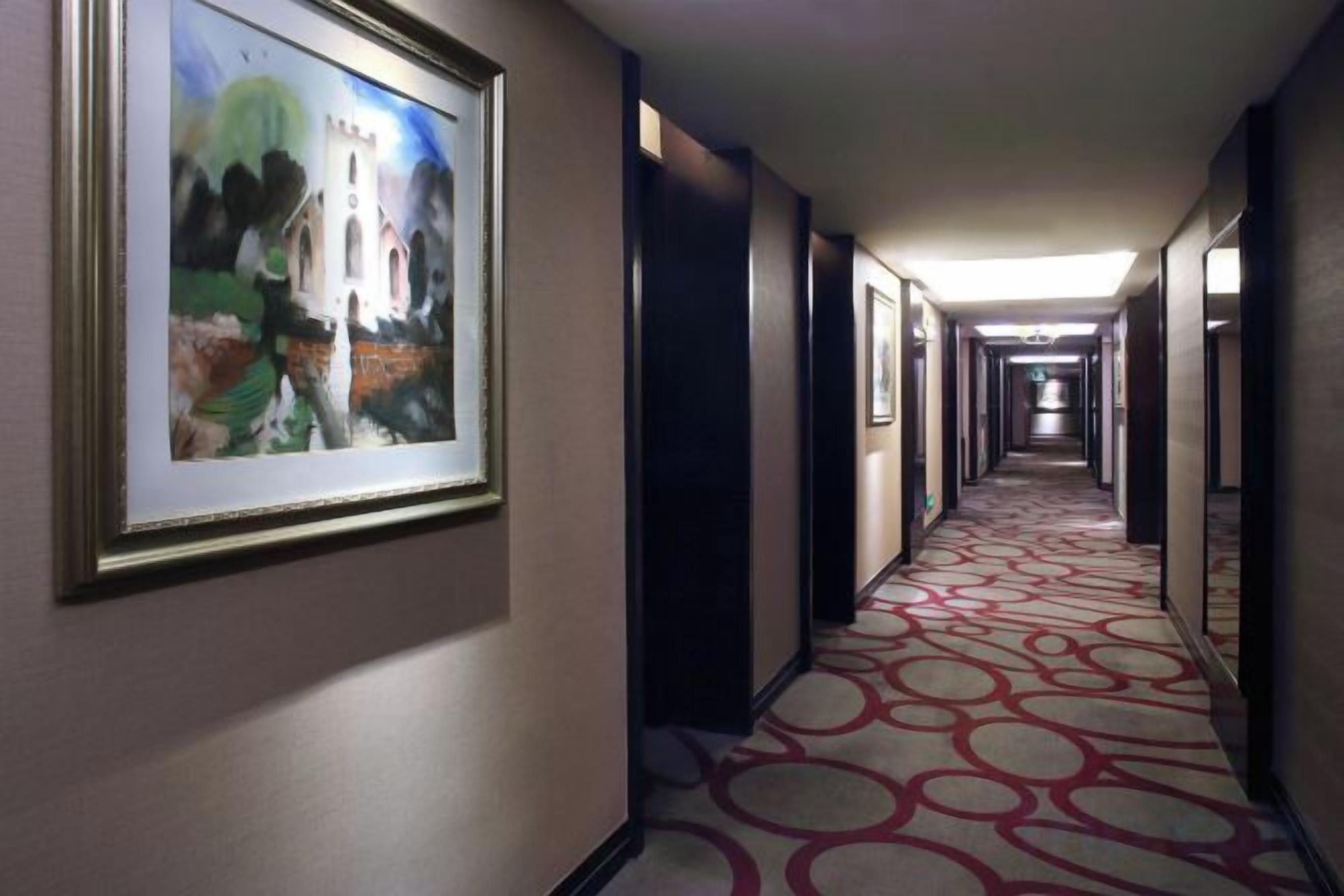 A hotel hallway with framed artwork on the walls, a patterned carpet, and doors leading to rooms.