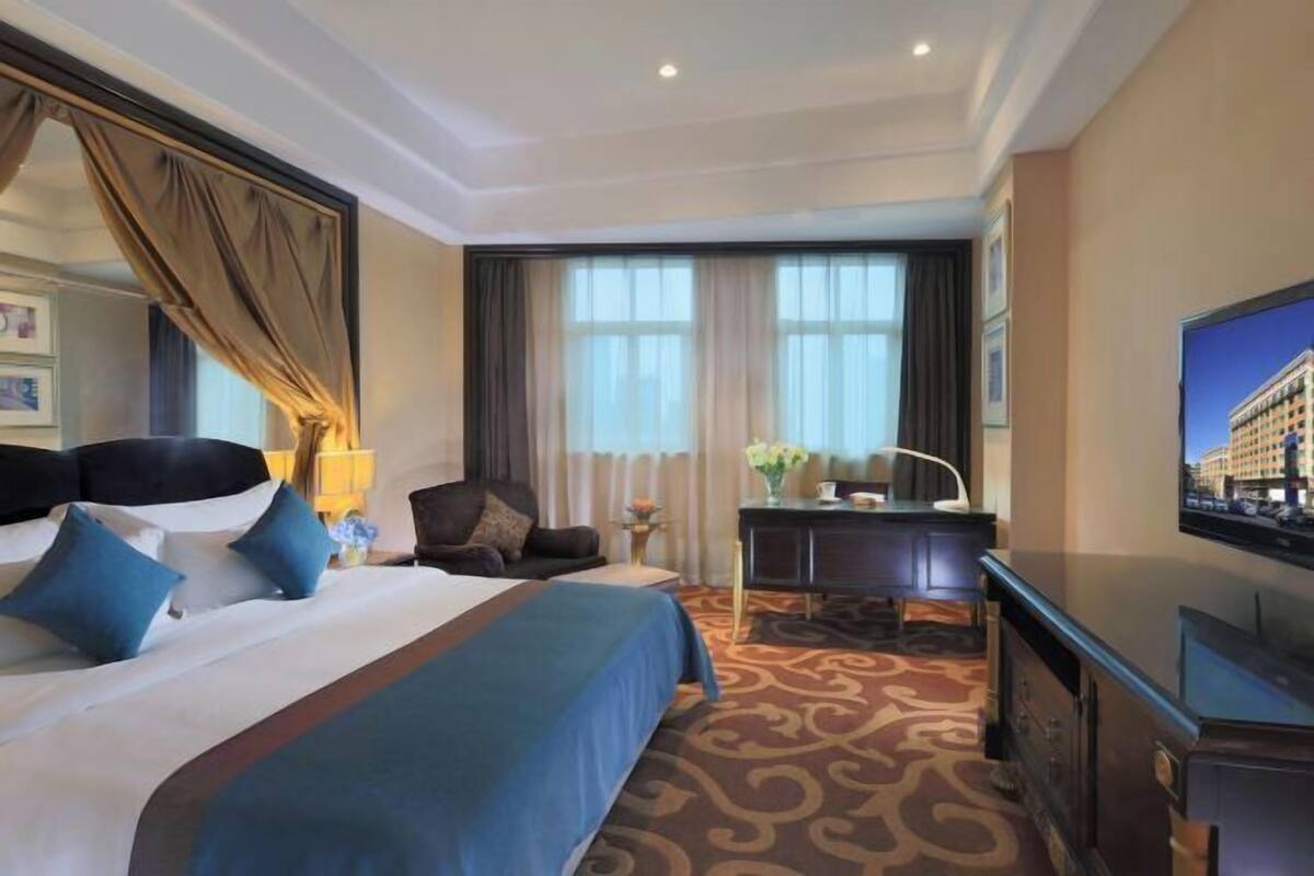 A hotel room with a large bed, a desk, a television, and a window with curtains.