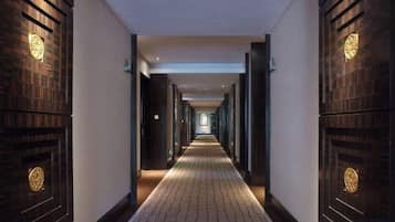 A long, narrow hallway with wooden doors on both sides, leading to a bright room at the end.
