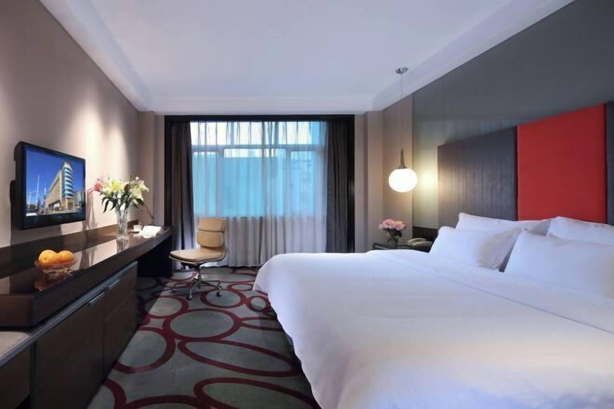A hotel room with a large bed, a desk with a chair, a television, and a window with curtains.