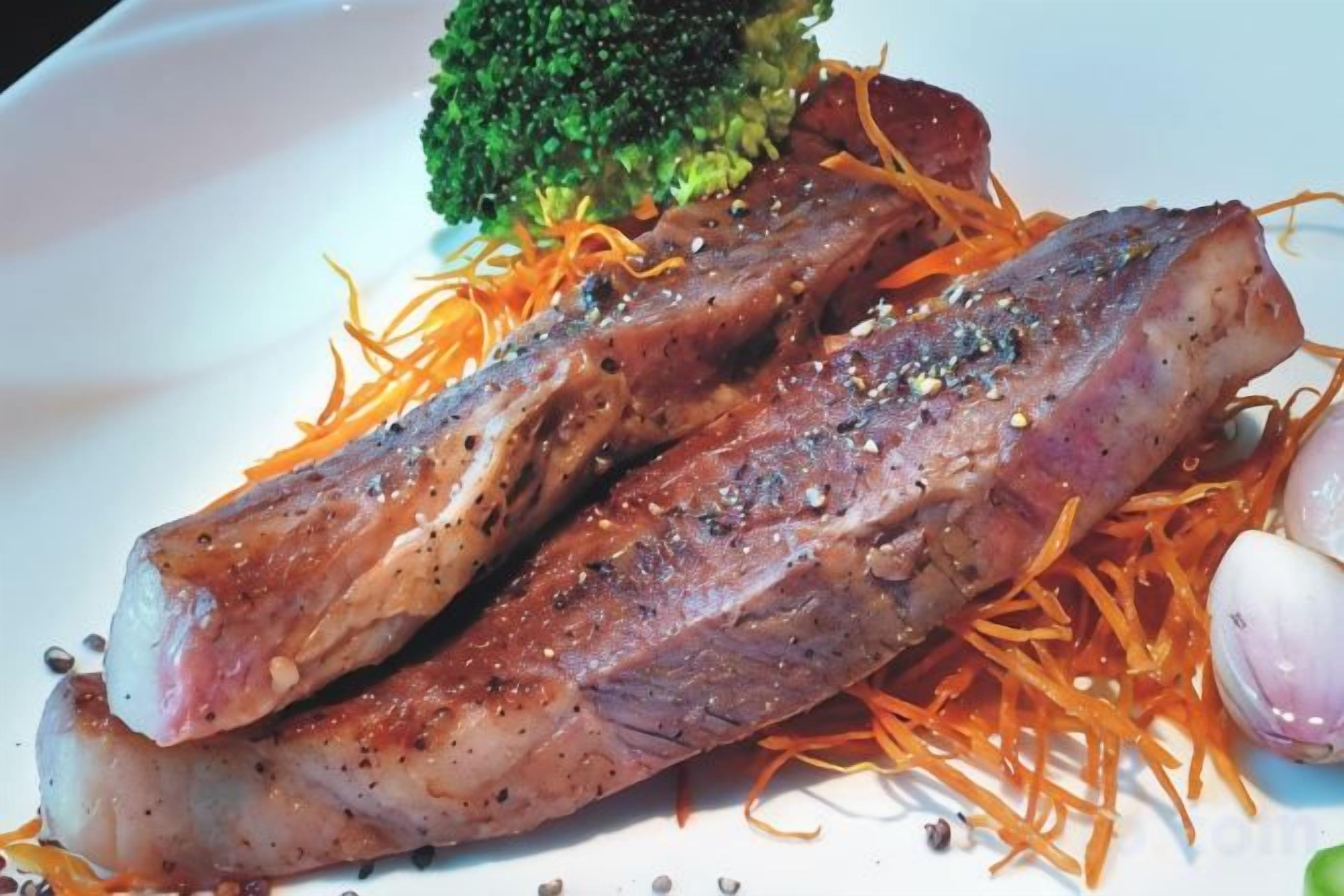A plate with a piece of meat, broccoli, and shredded carrots.