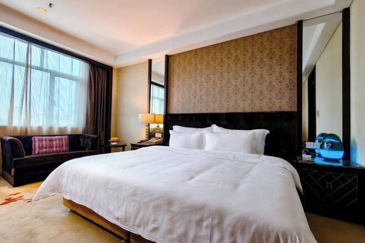 A hotel room with a large bed, a sofa, a nightstand, a lamp, and a large mirror.