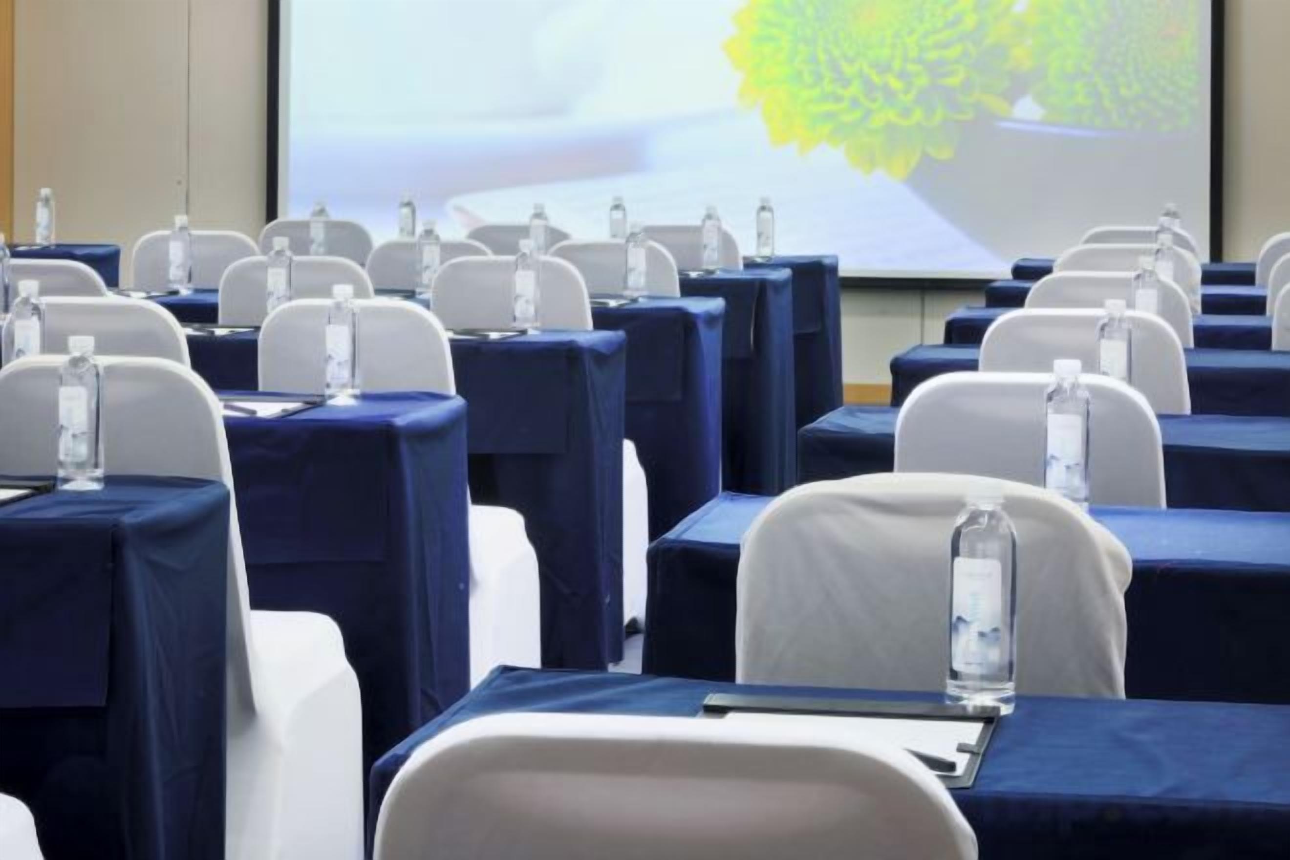 A conference room with rows of tables and chairs, each with a water bottle on the table.