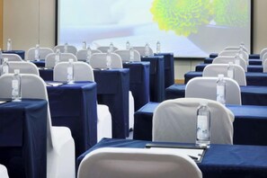 Une salle de conférence avec des rangées de tables et de chaises, chacune étant équipée d’une bouteille d’eau.
