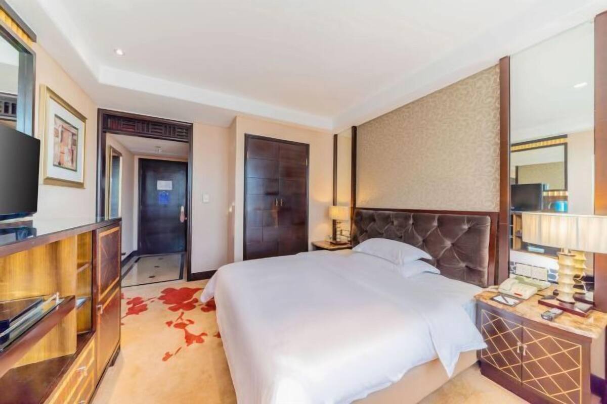 A hotel room with a large bed, a television, a desk with a lamp, and a wardrobe.