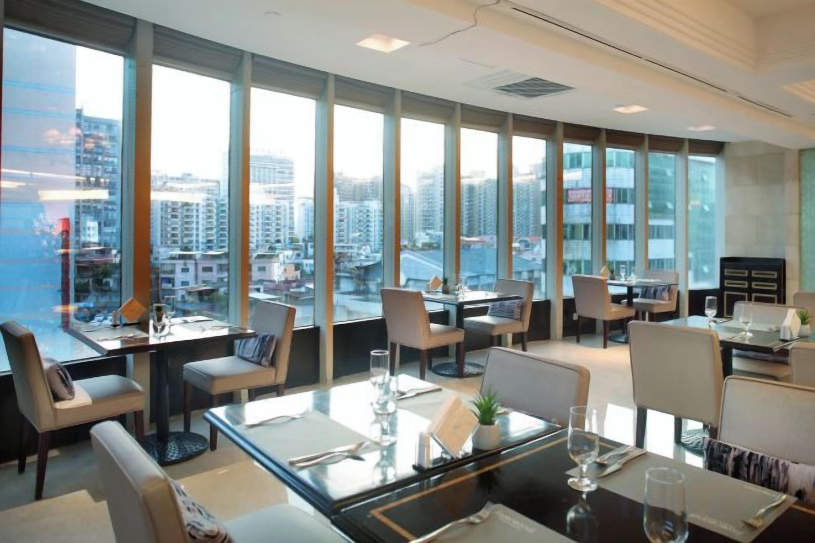 Un comedor de hotel moderno con amplias ventanas, varias mesas y sillas.