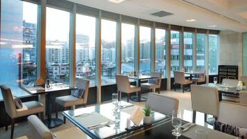 Un comedor de hotel moderno con amplias ventanas, varias mesas y sillas.