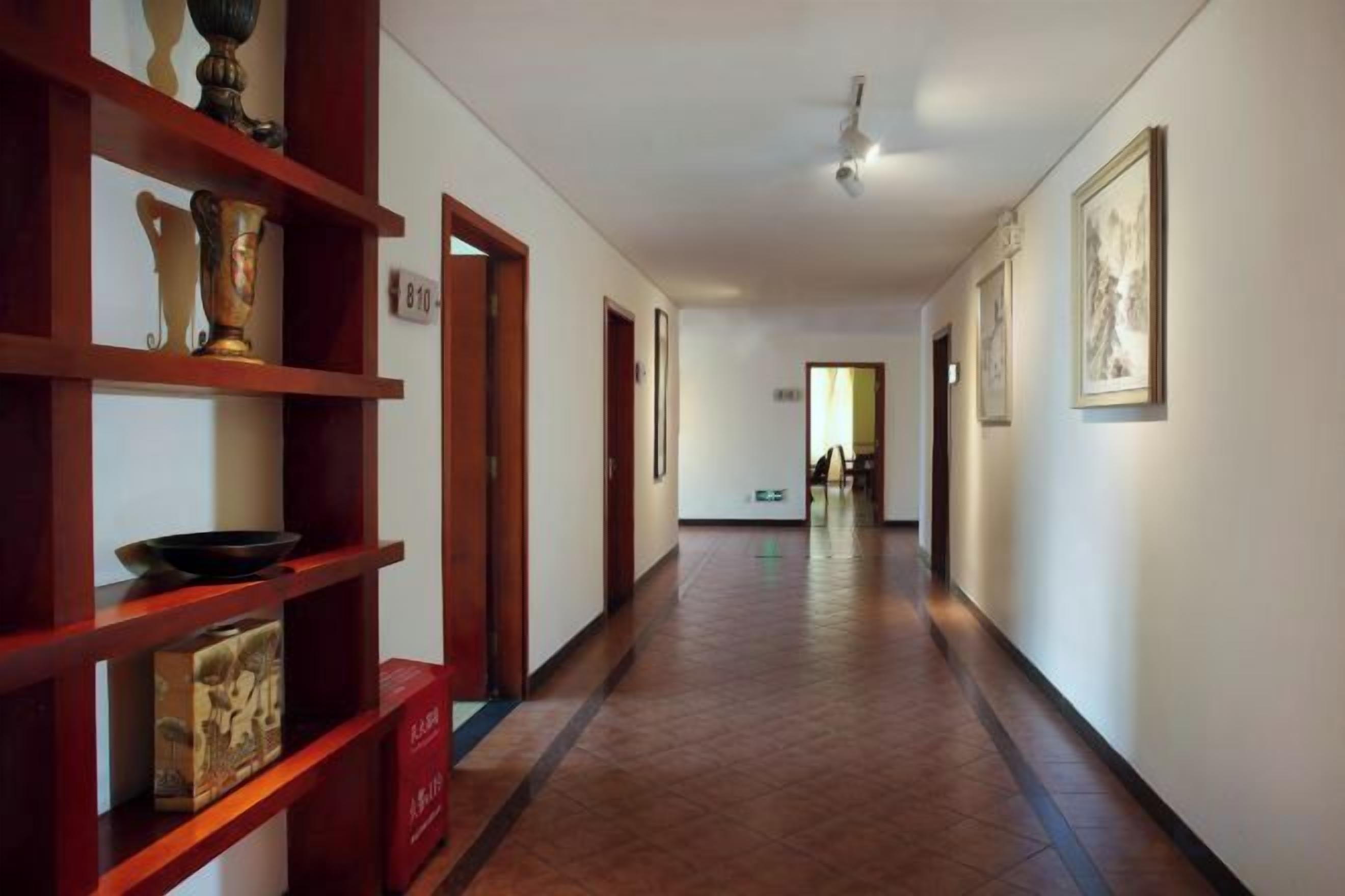 Un pasillo con estanterías de madera, puertas y cuadros en las paredes.