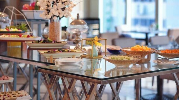 Uma mesa de buffet com diversos alimentos e um vaso decorativo de flores brancas.
