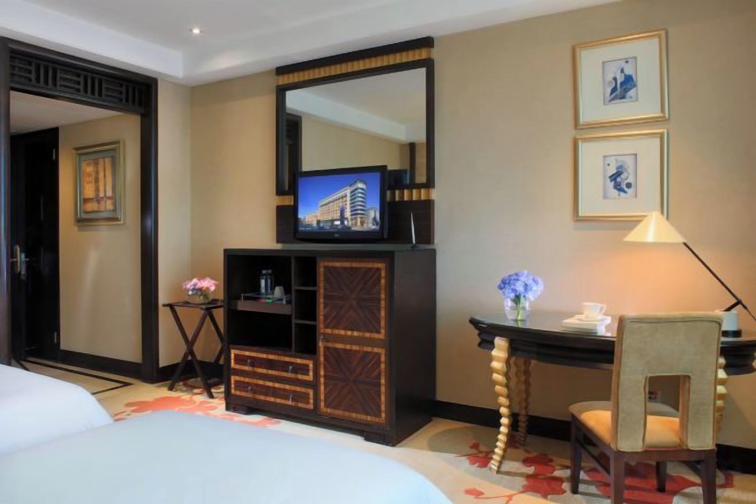 Une chambre d’hôtel équipée d’un lit, d’un bureau, d’une chaise, d’une télévision et d’un miroir.