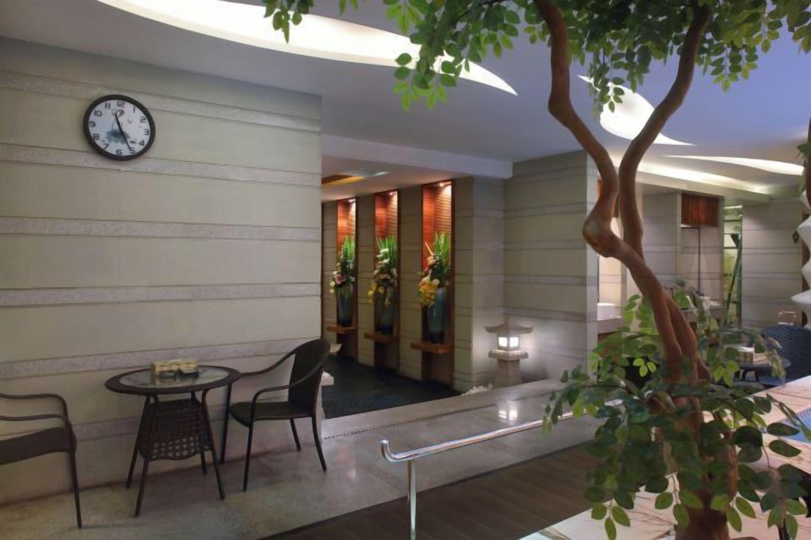A hotel lobby with a clock, seating area, and a plant.