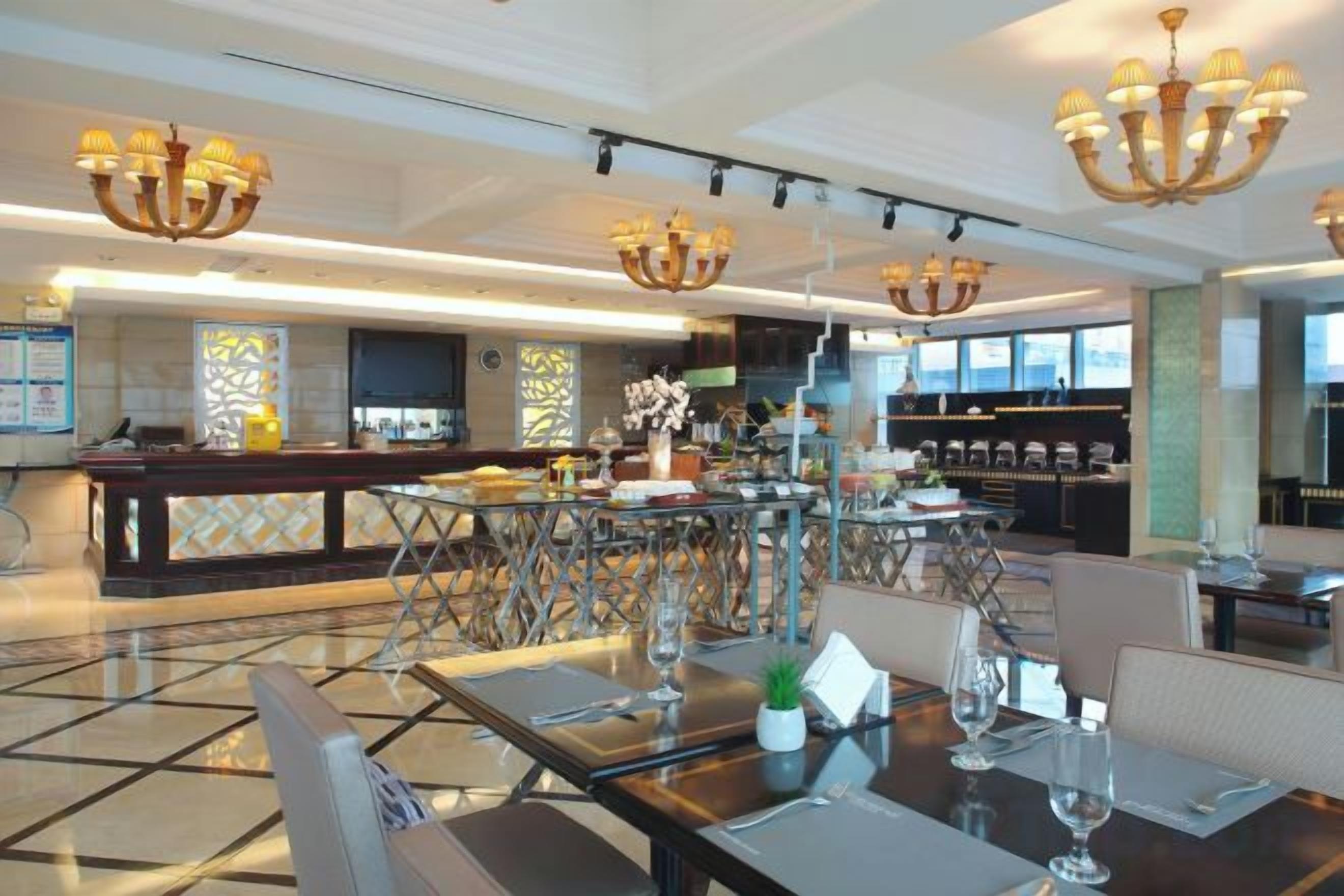 A spacious hotel lobby with a bar area, dining tables, and modern chandeliers.