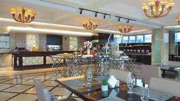A spacious hotel lobby with a bar area, dining tables, and modern chandeliers.