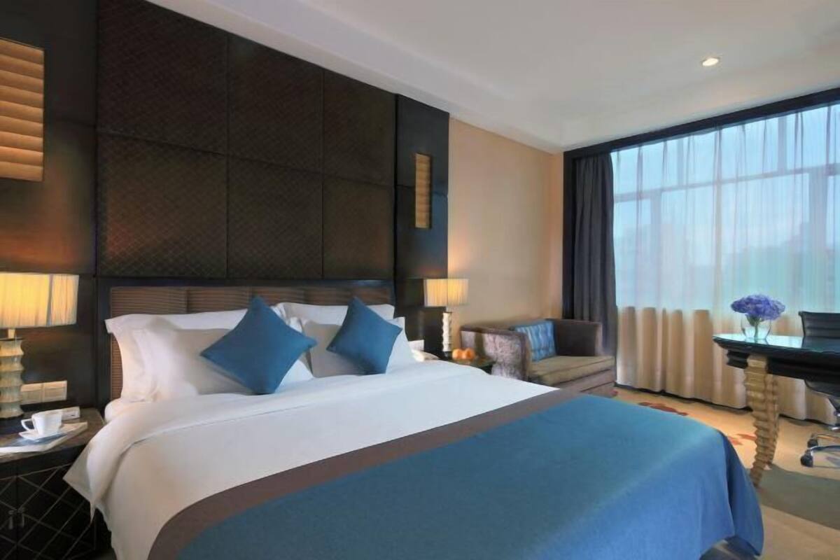 A hotel room with a large bed, a desk, a chair, and a window with curtains.
