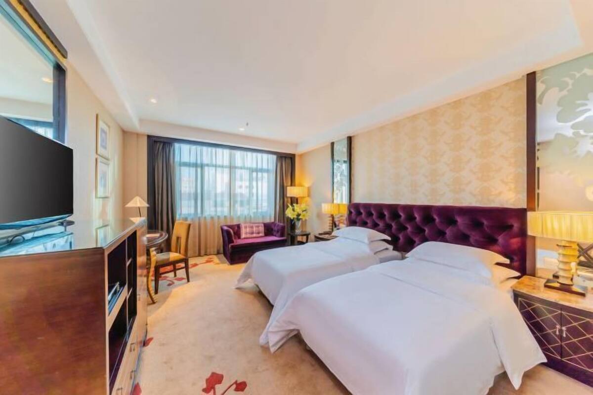 A hotel room with two beds, a TV, a desk, and a chair.