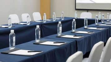 Un salón de conferencias con mesas dispuestas para una reunión, cada una con una botella de agua, un bloc de notas y un bolígrafo.