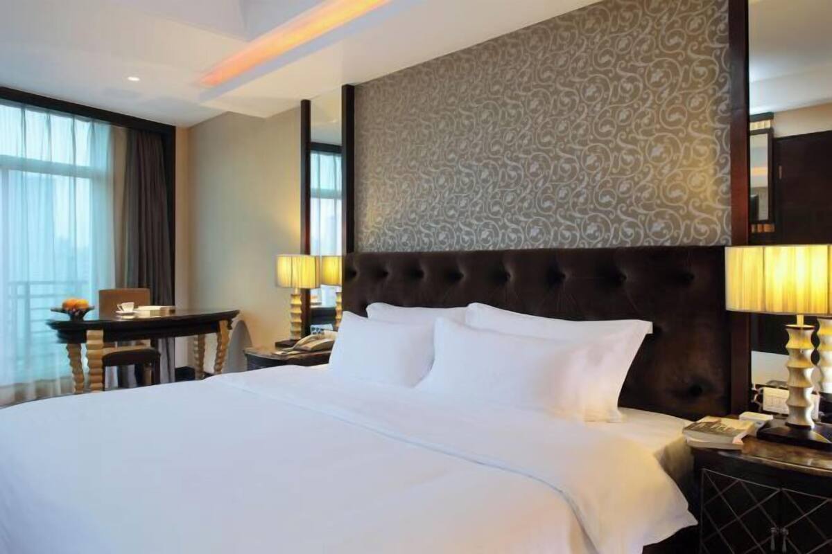 A hotel room with a large bed, a wooden nightstand, a desk, and a patterned wall.