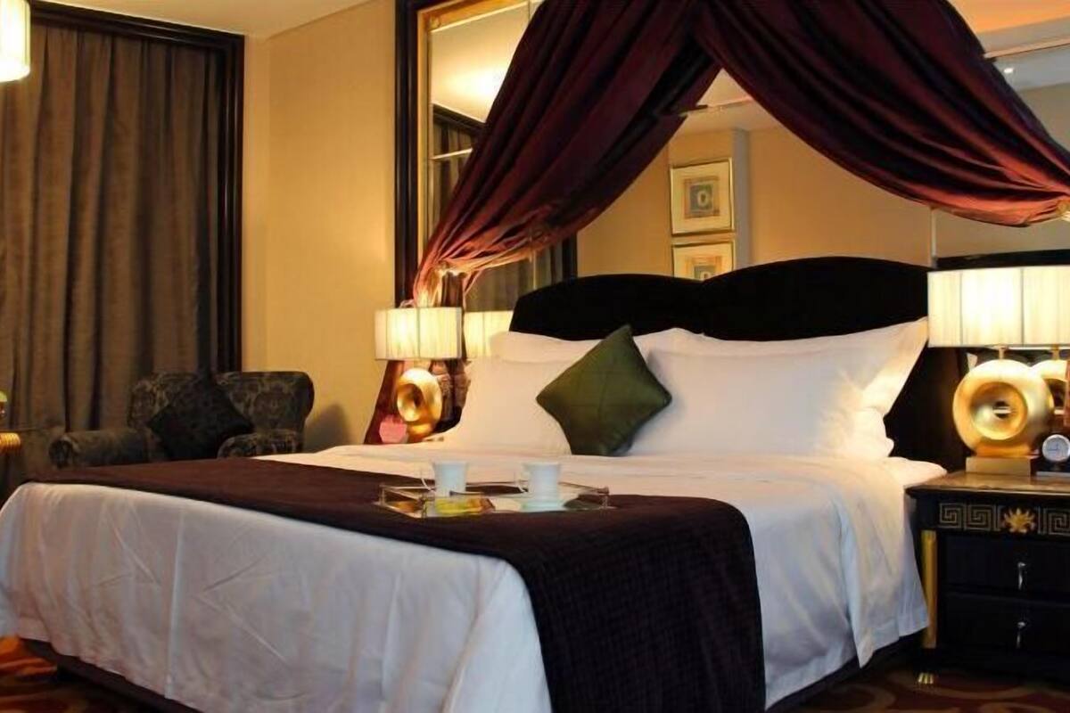A hotel room with a large bed, a canopy, a nightstand with a lamp, and a chair.