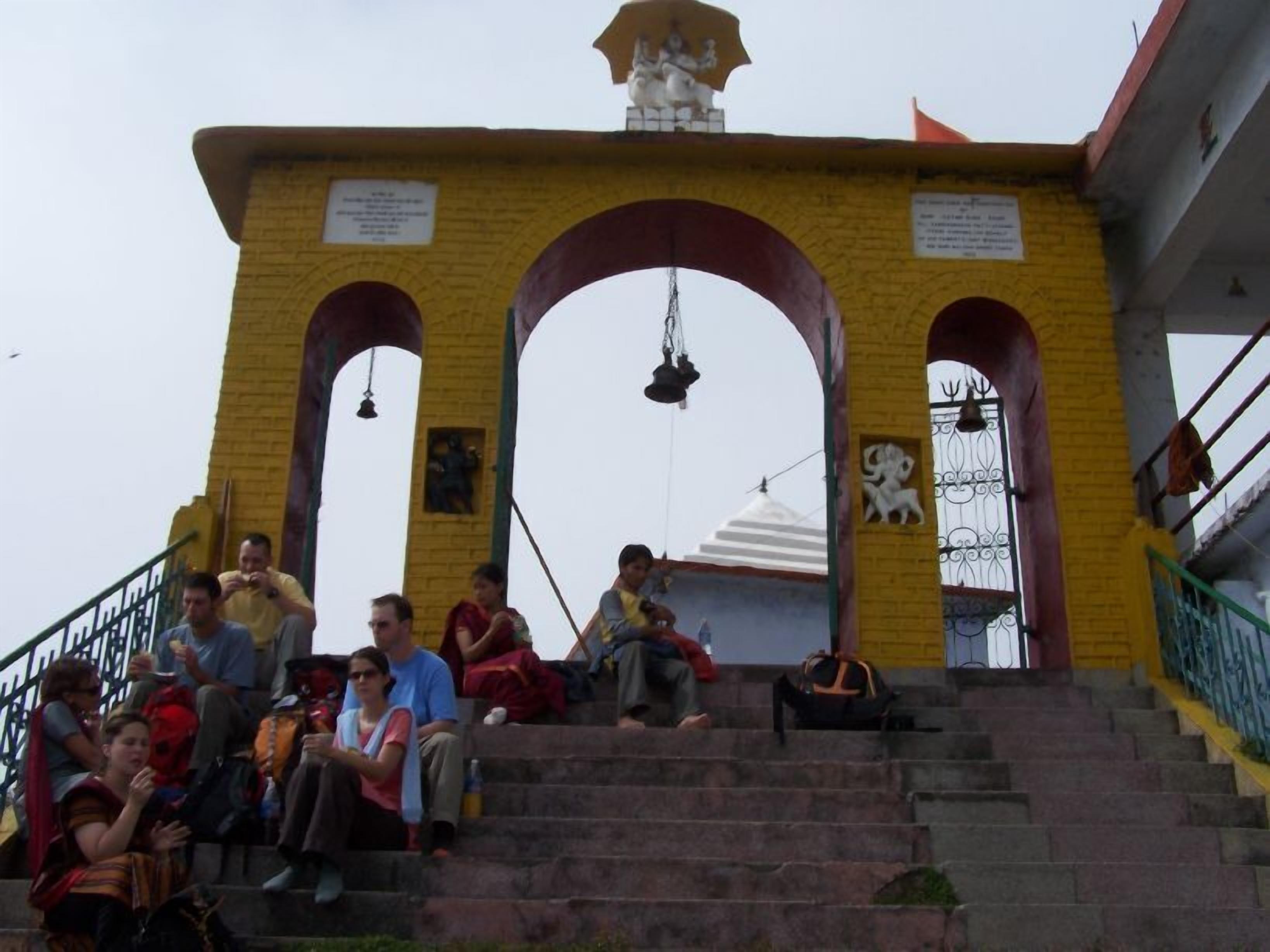 A temple entrance with steps leading up to a structure featuring a bell tower and a statue.