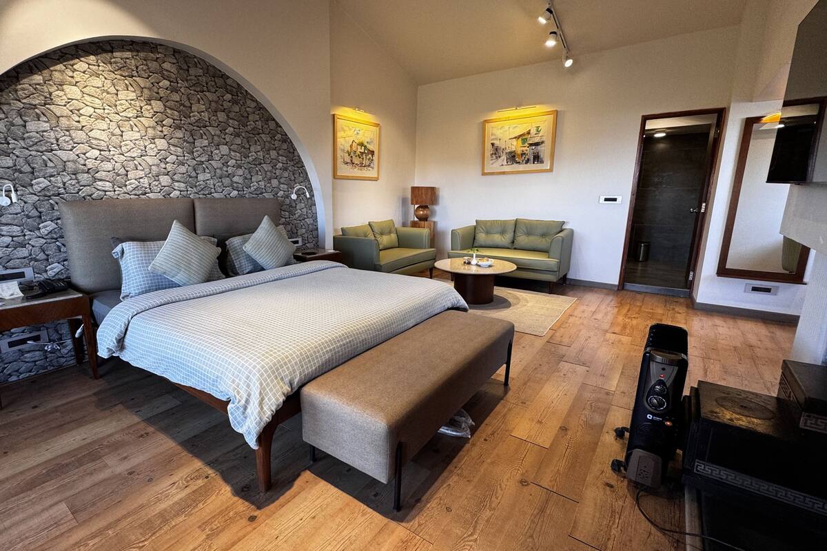 A bedroom with a stone wall arch, a bed with a checkered bedspread, a green sofa, a wooden coffee table, and a flat-screen TV.