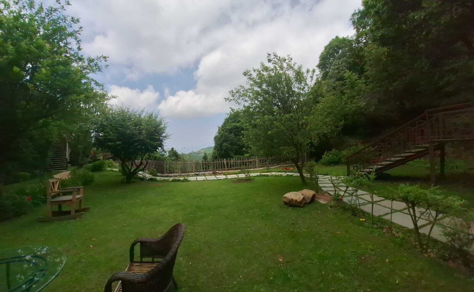 A grassy outdoor area with a wooden bench, a stone pathway, and a wooden staircase leading up a hill.