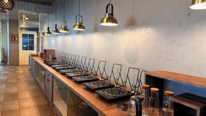 A kitchen with a long counter, multiple induction cooktops, hanging pendant lights, and a tiled floor.