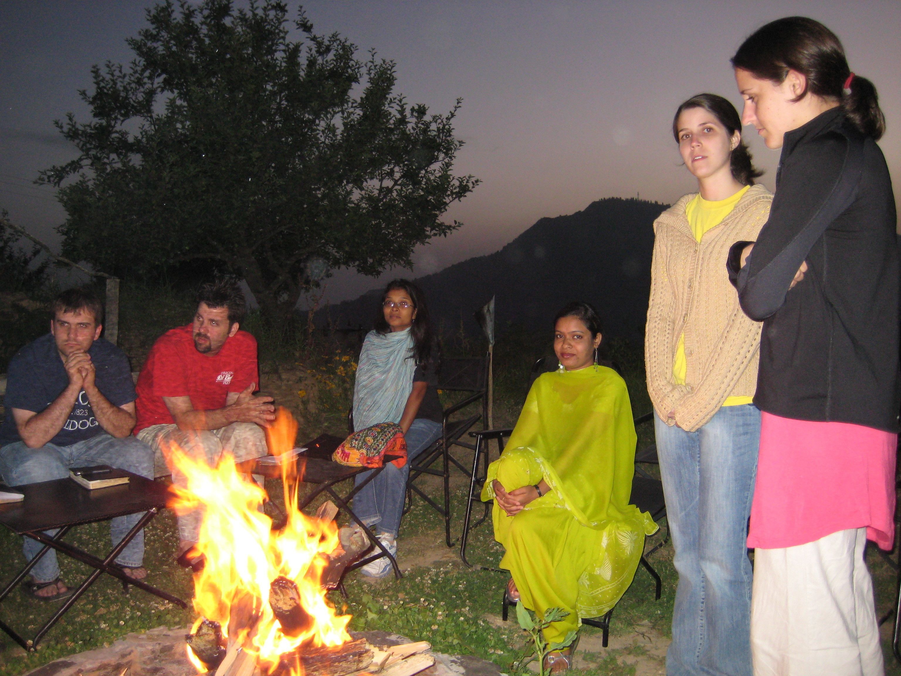 A group of people gathered around a campfire outdoors at dusk.