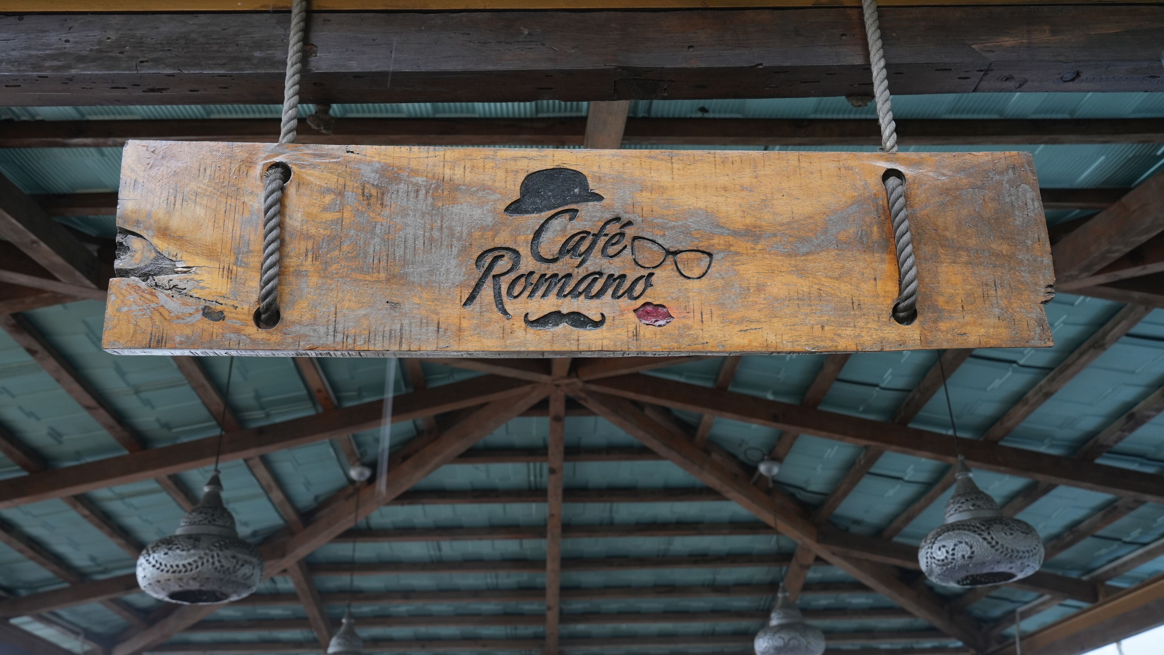 A rustic wooden sign with the text "Cafe Romano" and decorative elements like a hat and glasses.