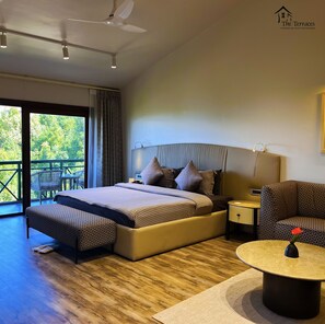 A modern hotel room with a large bed, a side table, a chair, and a balcony with outdoor furniture.