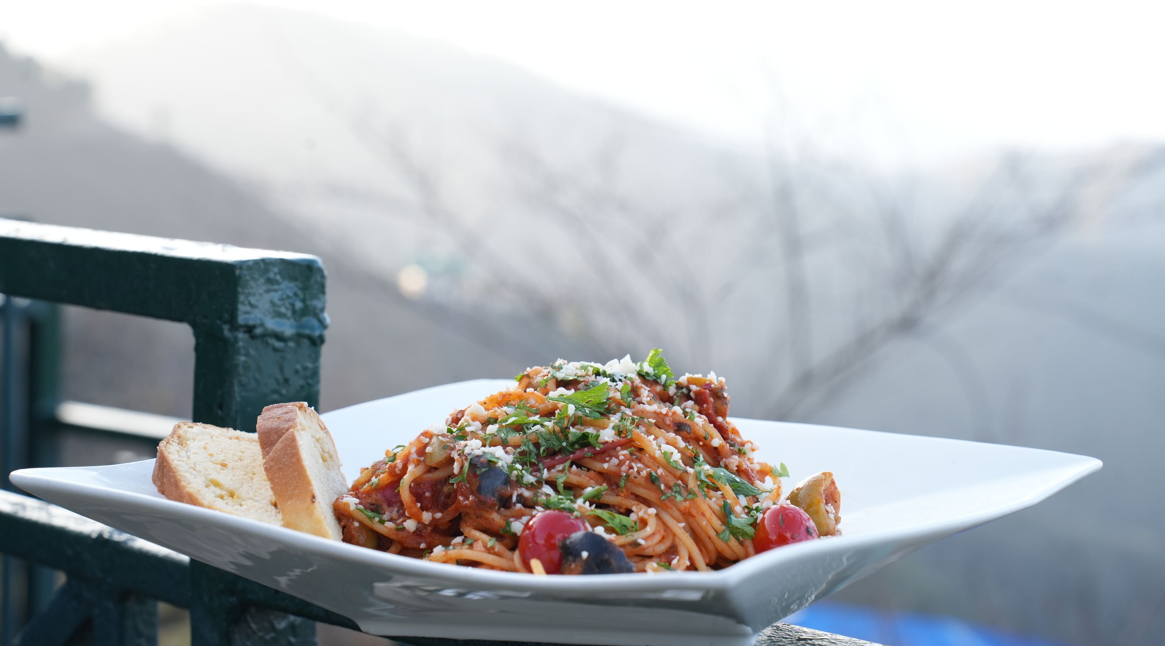A plate of spaghetti with tomato sauce, garnished with herbs and cheese, accompanied by a slice of bread on a white plate.