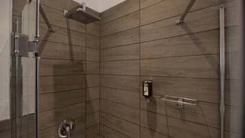 Une douche avec une porte en verre, un pommeau de douche amovible et un distributeur de savon.
