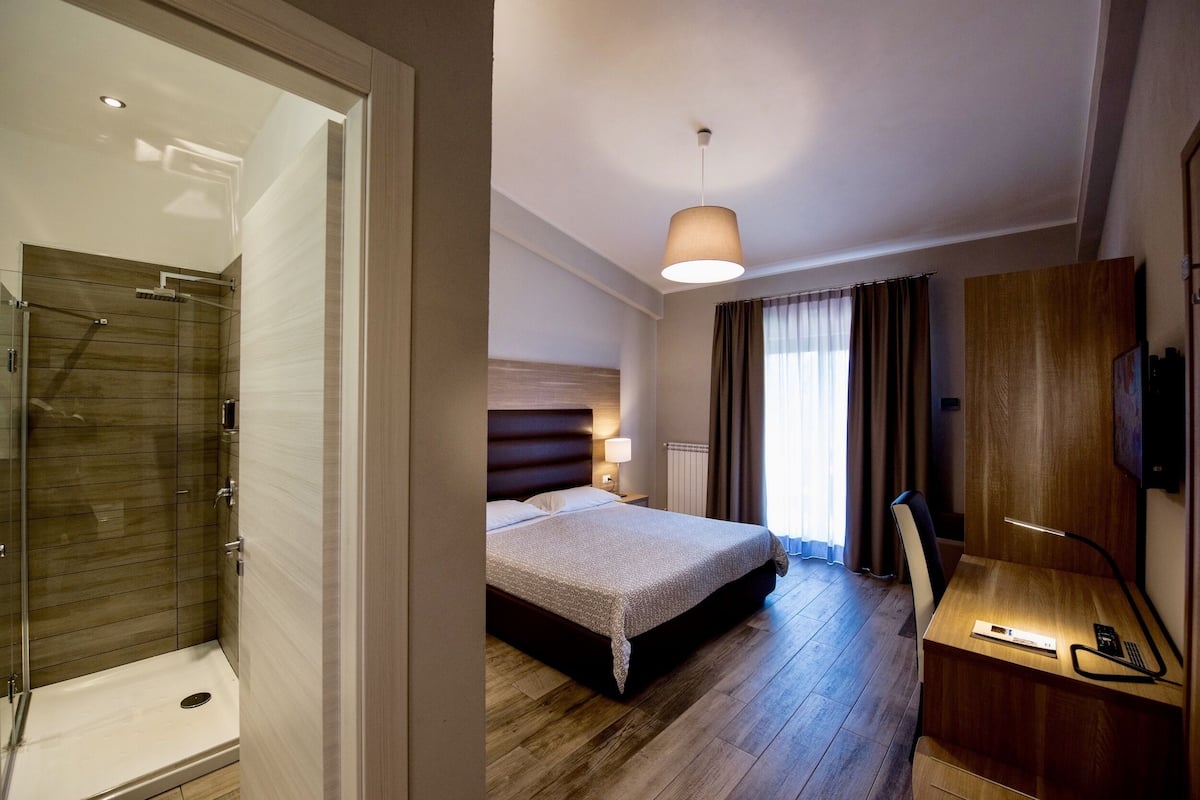 Ein Hotelzimmer mit Dusche, Bett, Schreibtisch und Fernseher.