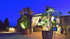 Un patio con plantas grandes en macetas, un edificio con techo de tejas y una pared de piedra.