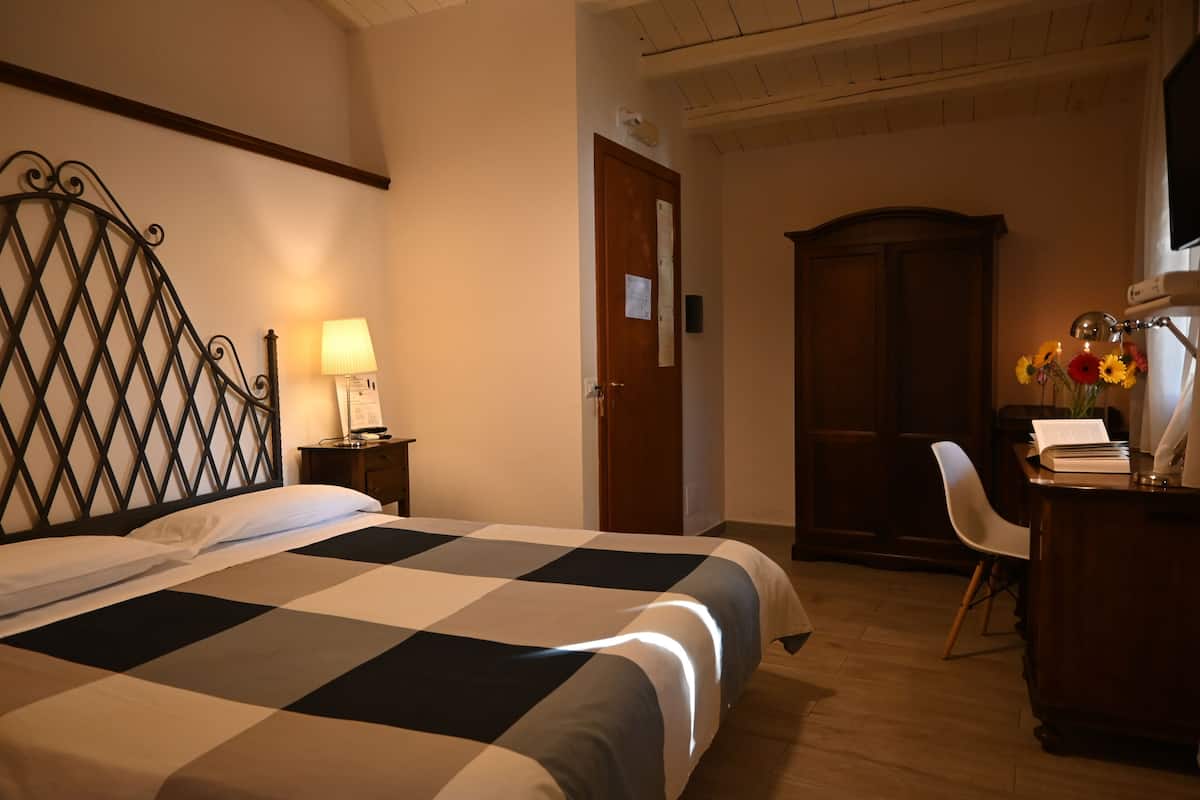 Ein Hotelzimmer mit kariertem Bettbezug, einem Schreibtisch mit Lampe, einem Stuhl und einem Holzschrank.