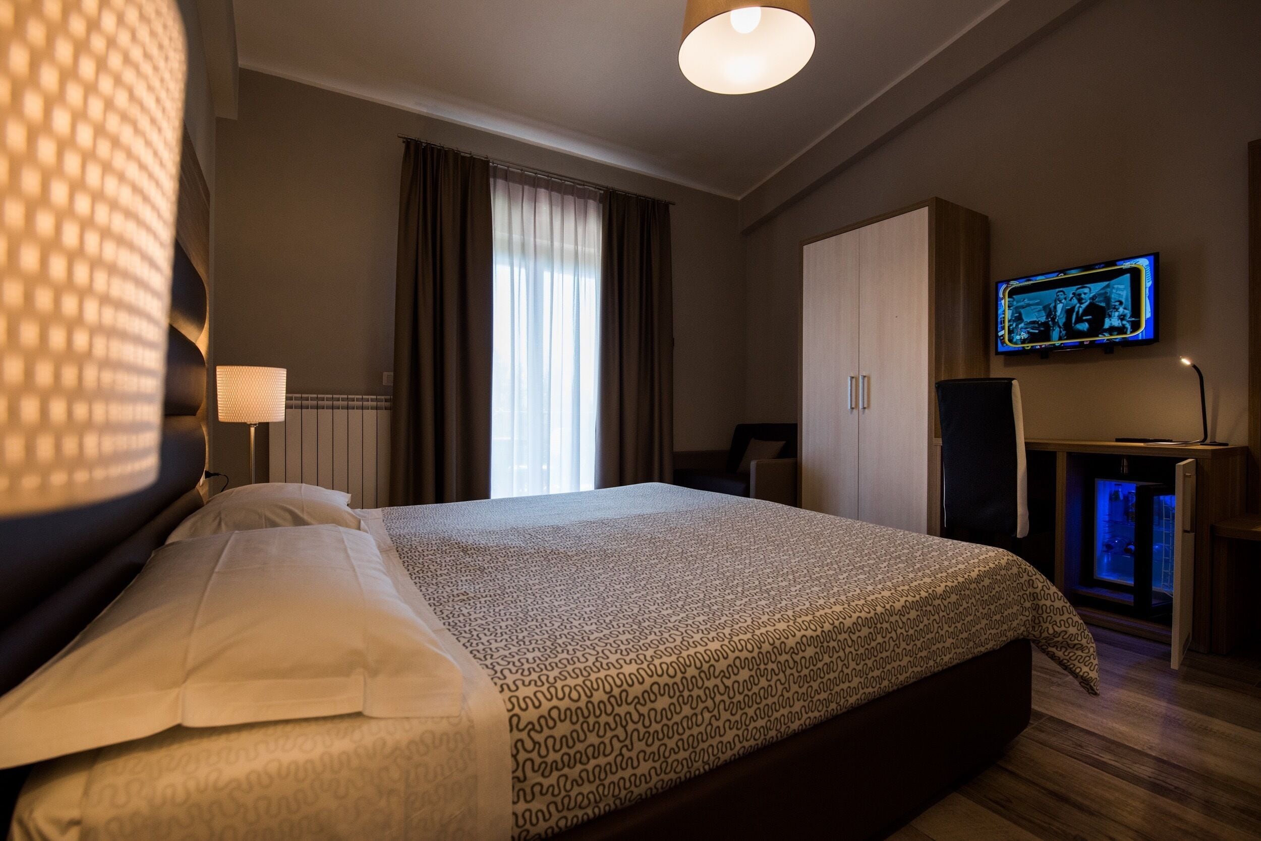 A hotel room with a large bed, a television on the wall, and a desk with a computer.