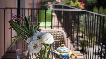 Un balcón con una mesa de madera, un florero de cristal transparente con flores blancas y dos tazas de cerámica con un diseño azul y amarillo.
