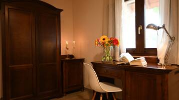 Un escritorio de madera con una silla blanca, un jarrón con flores, un libro abierto y una lámpara de escritorio.