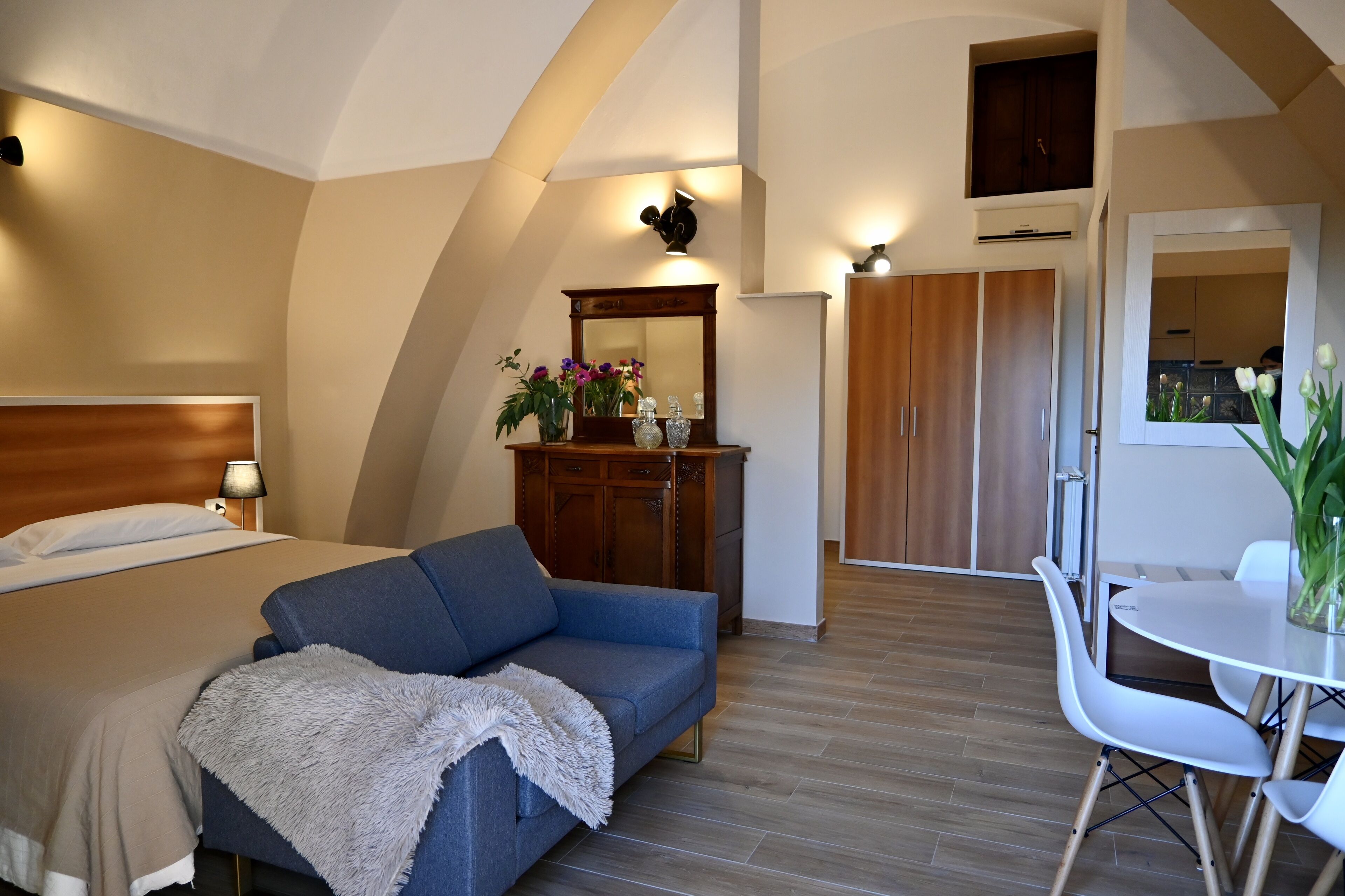 A bedroom with a bed, a sofa, a dining table, and a mirror.