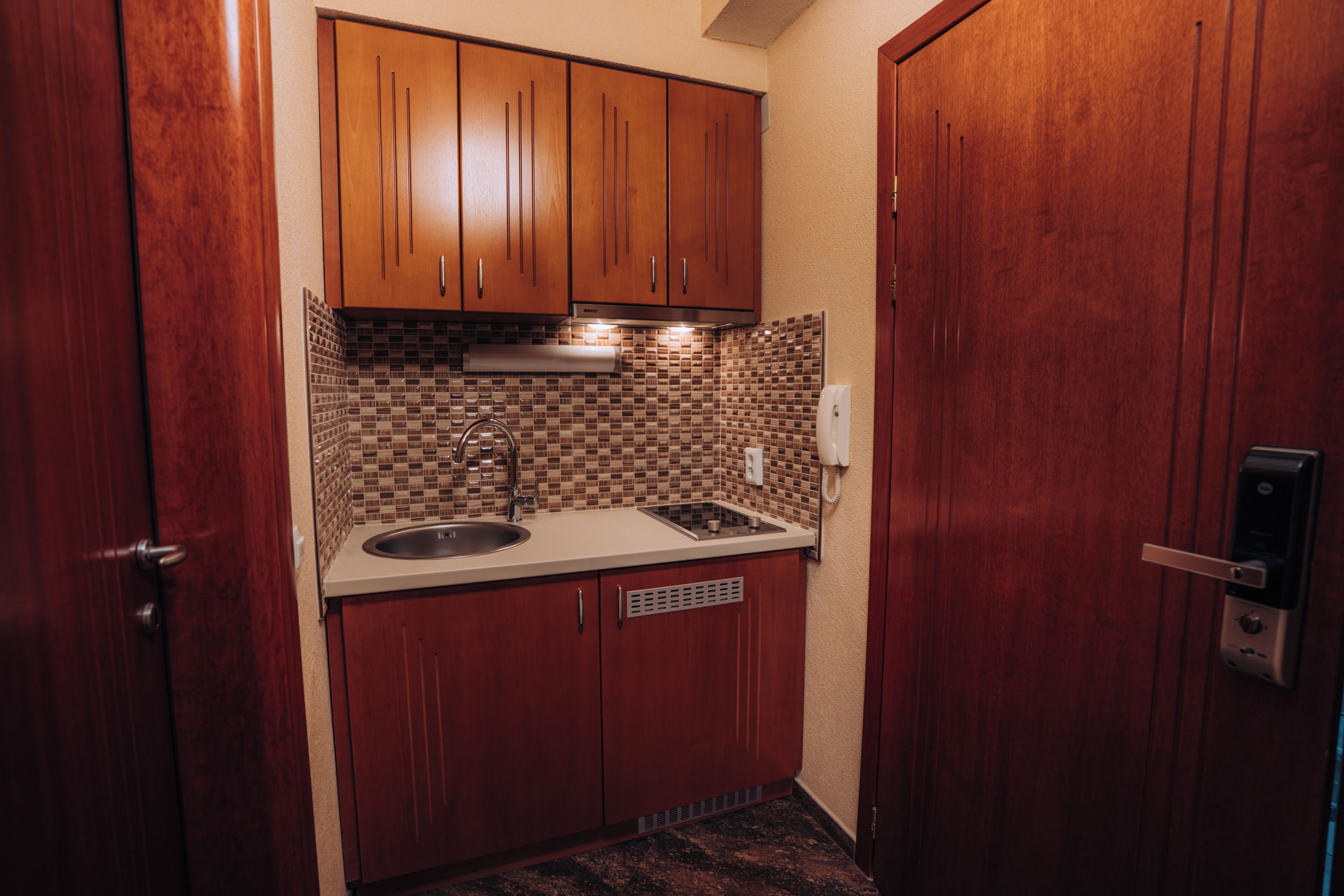 A compact kitchen with wooden cabinets, a tiled backsplash, a sink, and a stove.