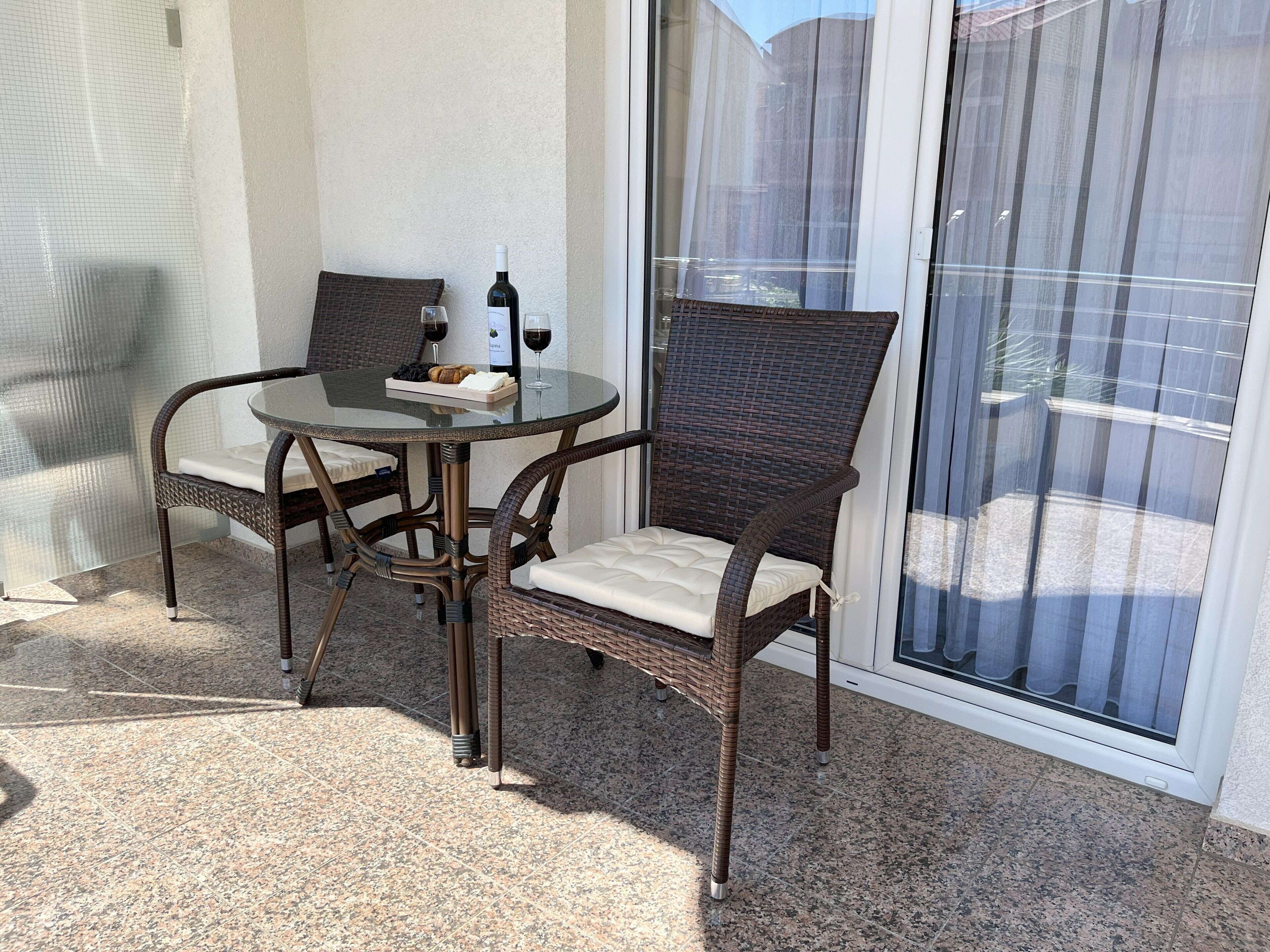 A patio with a glass table, wicker chairs, and a bottle of wine.