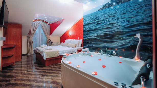 Een slaapkamer met een groot bed, een badkuip met rozenblaadjes en een muurschildering van een zeegezicht.